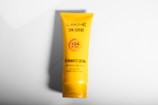 A yellow tube of Lakmé Sun Expert Ultramatte Lotion is placed against a plain white background. The product details indicate SPF 24 and PA++, highlighting its lightweight, non-sticky formula suitable for all skin types. The design is minimalistic, focusing on the brand and product benefits.