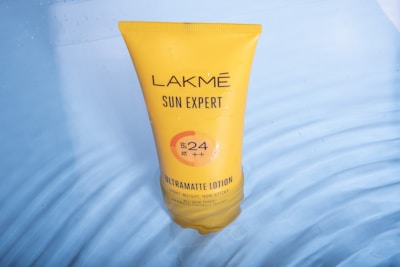 A yellow tube of Lakmé Sun Expert Ultra Matte Lotion is submerged in clear water. The tube displays information about its SPF 24 and PA rating.