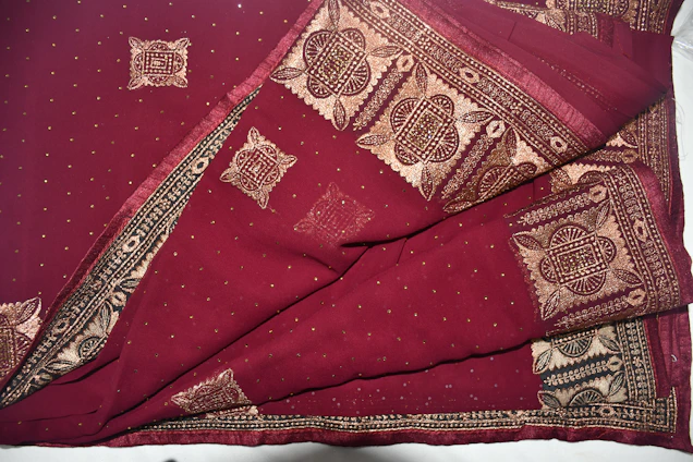 A close-up of a luxurious maroon embroidered fabric with antique gold threadwork, highlighting intricate craftsmanship.
