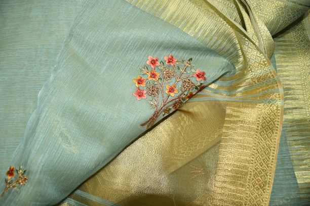 A close-up of a delicate pink fabric with gold thread embroidery, showcasing fine stitching craftsmanship.