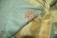 A close-up of an elegant fabric featuring intricate floral embroidery. The fabric consists of a blend of soft blue and golden tones, with detailed red flower designs woven into it. The texture appears rich and smooth, highlighting the fine craftsmanship.