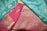 Luxurious fabrics with intricate patterns and embroidery in vibrant colors. One piece is teal with gold motifs, while the other is a rich pink with detailed geometric and floral patterns in gold thread.