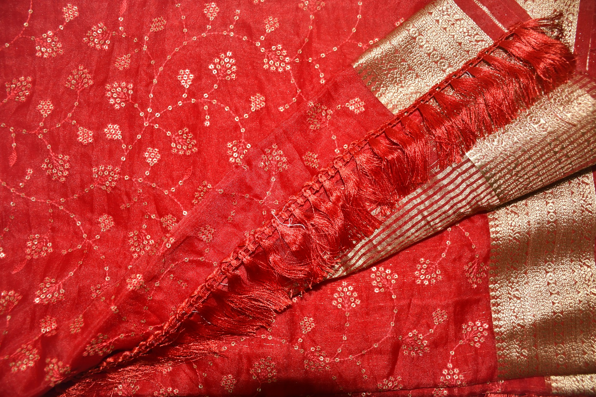 Close-up of a richly embroidered burgundy fabric showcasing intricate gold zari patterns with delicate floral motifs.