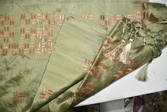Printed viscose fabric with intricate green and gold patterns displayed on a table.