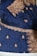 A rich blue fabric adorned with intricate gold embroidery, featuring floral and paisley patterns. The ornate designs are meticulously stitched with glittering gold thread, highlighting an elaborate and traditional textile craftsmanship.
