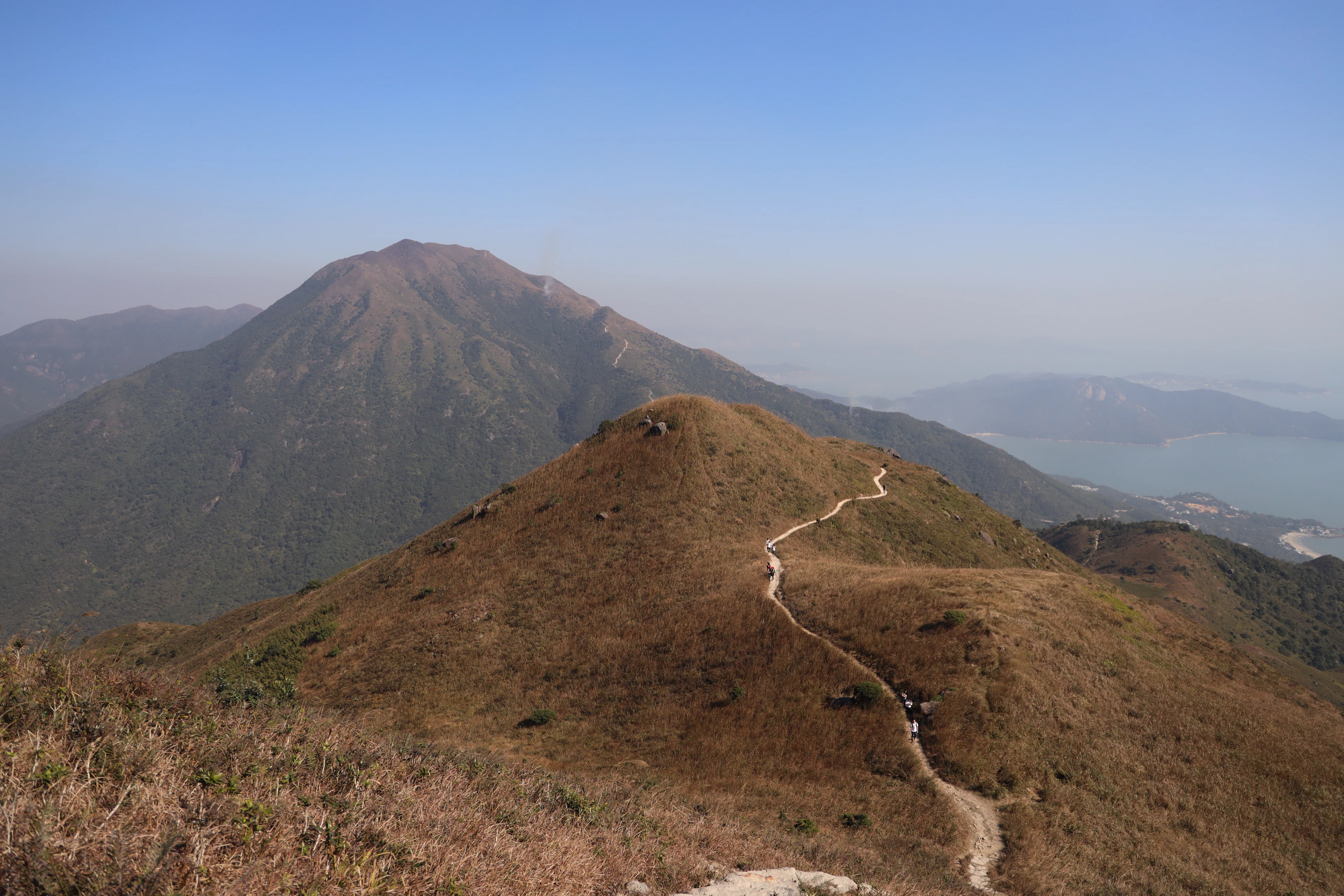 A trail winding along a ridge of dry winter grass above the sea in Hong Kong