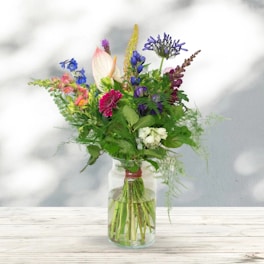 A vibrant bouquet of mixed pastel flowers arranged elegantly in a clear glass vase.