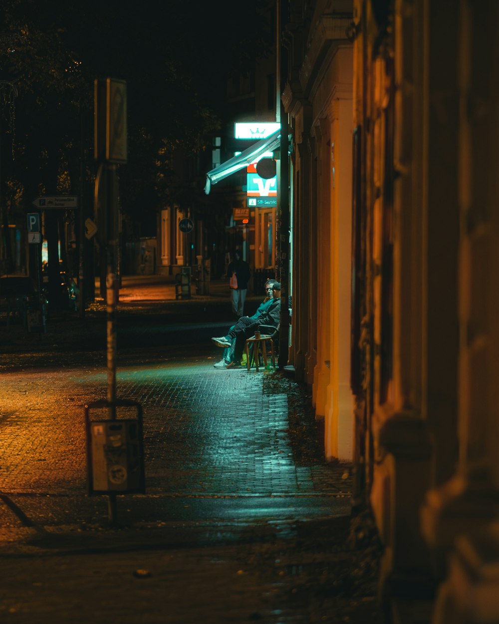 a person sitting on a bench on a city street at night