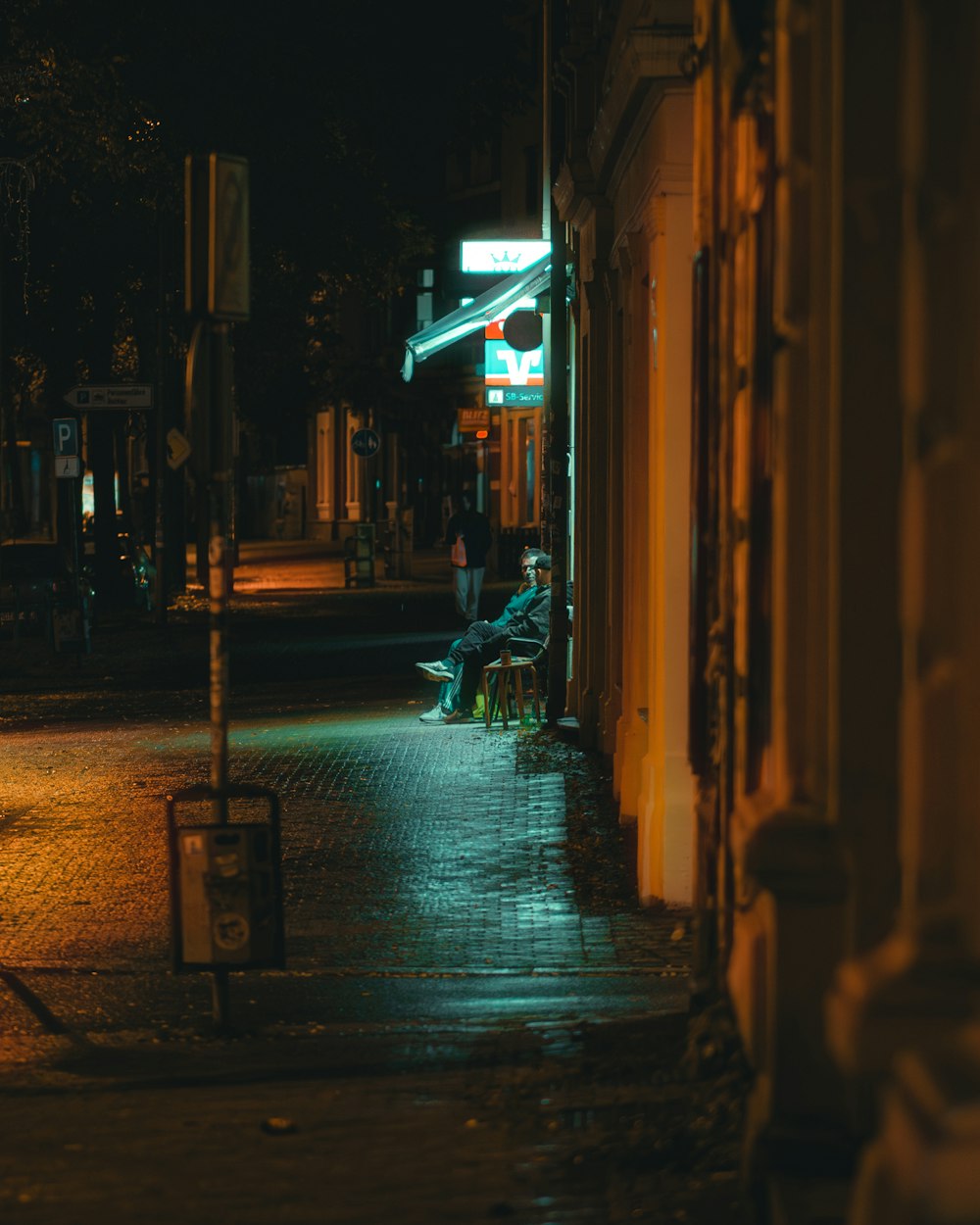 una persona sentada en un banco en una calle de la ciudad por la noche
