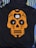 A black hoodie features an orange skull design in the style of a sugar skull with floral and heart embellishments. Positioned at the center of the design is a white charging case for wireless earbuds, with each earbud placed in the eyes of the skull. The hoodie is laid out on a background of striped and solid-colored fabrics.