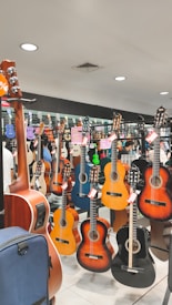 A music store display featuring various acoustic guitars hanging on racks. The guitars range in color, including natural wood tones, black, and blue. Several price tags are attached to the guitars, indicating a sale. The background reflects the inside of a music shop with bright lighting and mirrors enhancing the display.