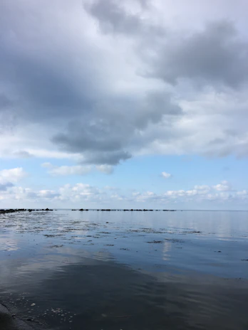 Horizontal view of a calm sea with distant waves blending into a cloudy sky.
