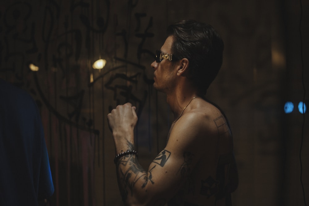 a man with tattoos standing in front of a wall