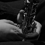 Black and white portrait of Jaiden holding his saxophone, framed by soft shadows.