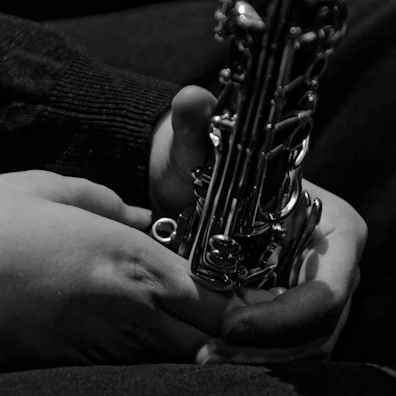 Black and white portrait of Jaiden holding his saxophone, framed by soft shadows.