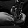 Hands holding and playing a saxophone, captured in close-up black and white photography.