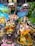 Two elaborately dressed deities are adorned with vibrant floral garlands, intricate jewelry, and colorful outfits. The background features a painted mural of nature with peacocks and trees, adding to the festive and sacred atmosphere.