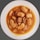 A bowl of stew with large white beans and chunks of sausage in a brown sauce, served on a white plate. The dish has a hearty and rustic appearance.