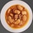 A bowl of stew with large white beans and chunks of sausage in a brown sauce, served on a white plate. The dish has a hearty and rustic appearance.