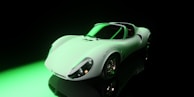 A sleek, vintage sports car with a smooth, curved body and prominent wheel arches under dramatic lighting. Reflections on the glossy surface suggest a highly polished finish. The setting is dark, with a green light highlighting part of the car, contributing to a mysterious and sophisticated atmosphere.