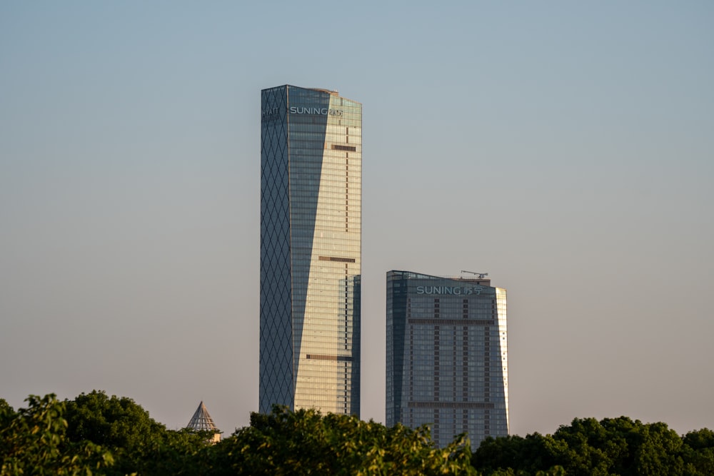 two tall buildings with trees in front of them