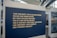 A large blue panel featuring a motivational quote in bold, yellow text is displayed at an exhibition. The quote encourages resilience and pride, specifically referencing Wembley. The area surrounding the panel includes other display stands and large windows.