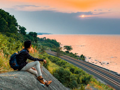 A serene travel scene showing a man with a backpack overlooking a coastal landscape at sunset.