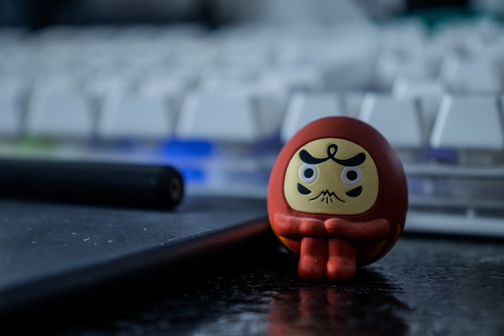 a red toy sitting on top of a desk next to a keyboard