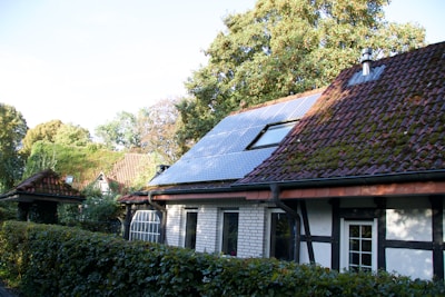 A cozy home bathed in sunlight with solar panels on the roof, surrounded by green trees.