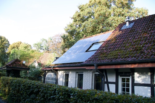 A cozy home with solar panels on the roof, surrounded by lush greenery.