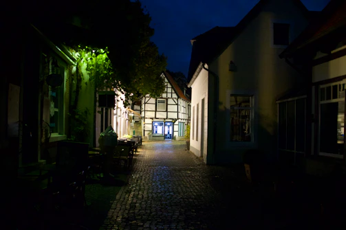 A quiet cobblestone alley lined with charming shops and glowing lanterns at dusk.