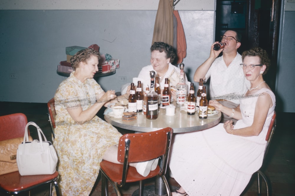 a group of people sitting around a table with bottles of beer