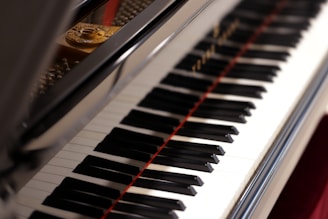 A close-up view of a piano keyboard with its shiny black and white keys, reflecting light. The open lid of the piano reveals some of the strings and the interior components.