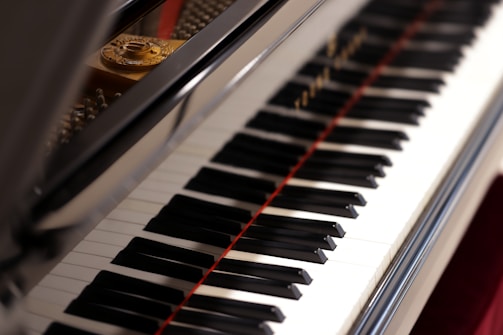 A close-up view of a piano keyboard with its shiny black and white keys, reflecting light. The open lid of the piano reveals some of the strings and the interior components.