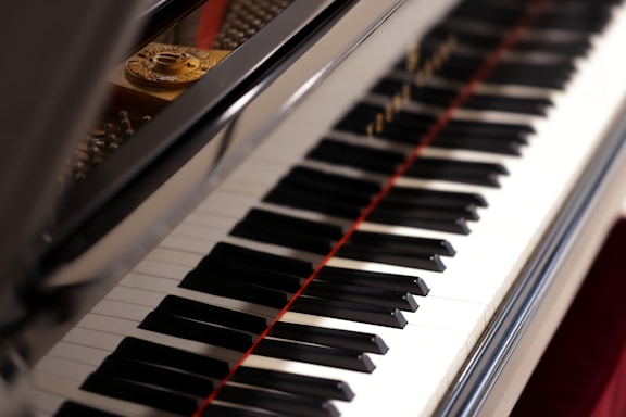 A close-up view of a piano keyboard with its shiny black and white keys, reflecting light. The open lid of the piano reveals some of the strings and the interior components.