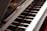 A close-up view of a piano keyboard with its shiny black and white keys, reflecting light. The open lid of the piano reveals some of the strings and the interior components.