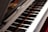 A close-up view of a piano keyboard with its shiny black and white keys, reflecting light. The open lid of the piano reveals some of the strings and the interior components.