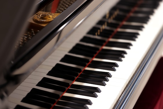 A close-up view of a piano keyboard with its shiny black and white keys, reflecting light. The open lid of the piano reveals some of the strings and the interior components.