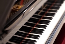 A close-up view of a piano keyboard with its shiny black and white keys, reflecting light. The open lid of the piano reveals some of the strings and the interior components.