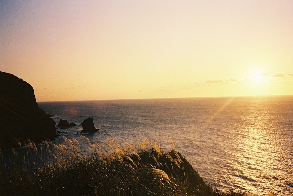 the sun is setting over the ocean on a cliff