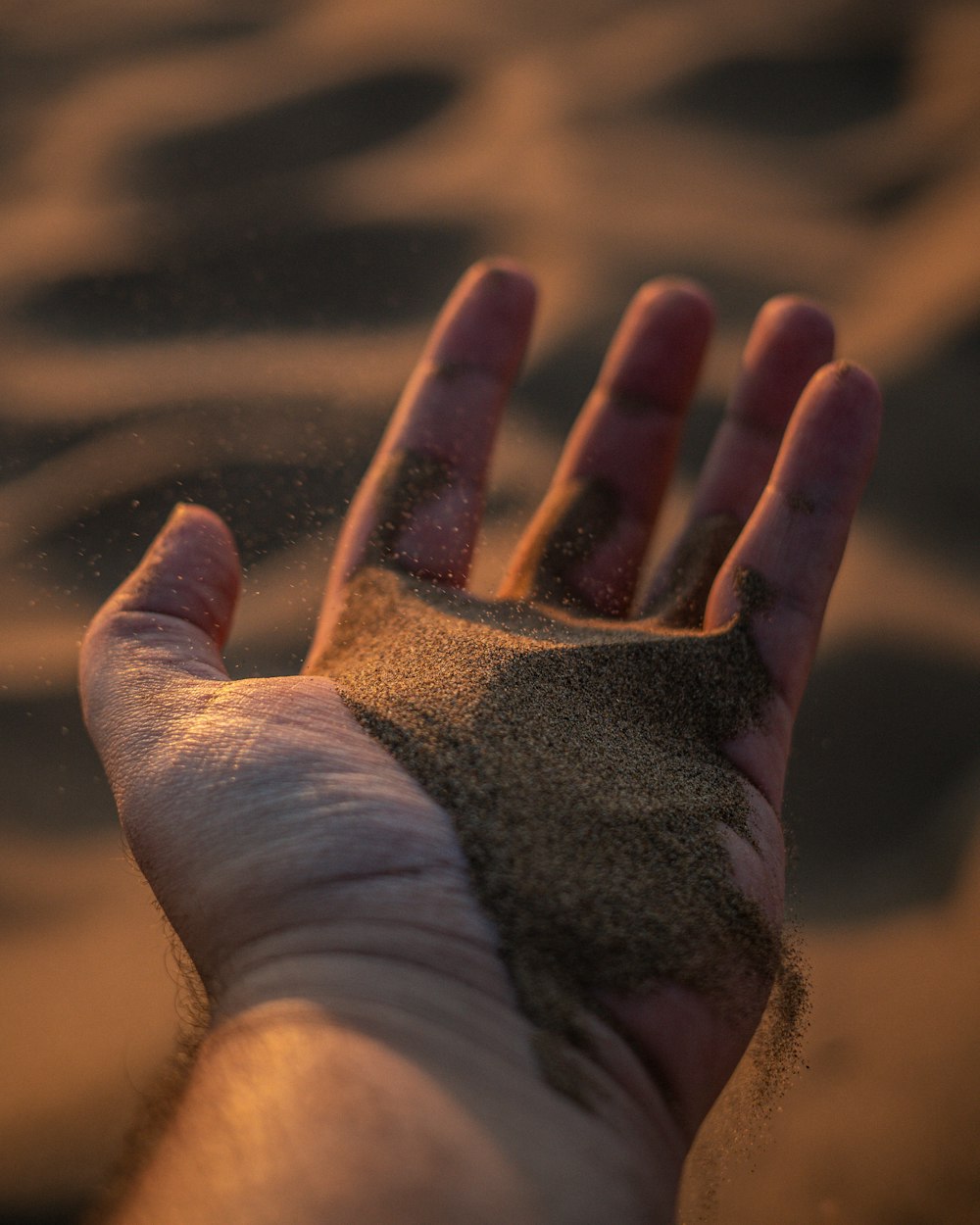 a hand holding sand in the sand on the beach