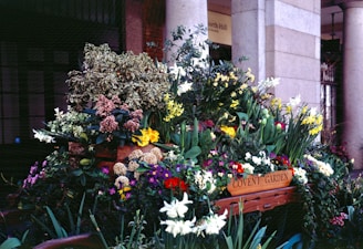 A rustic wooden cart overflowing with freshly cut flowers, set against a backdrop of garden beds.