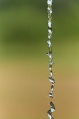 A stream of water suspended in mid-air set against a blurred green and brown background.