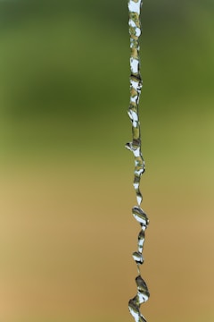 A stream of water suspended in mid-air set against a blurred green and brown background.