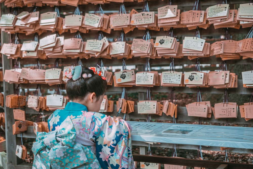 a woman in a kimono looking at a wall of wooden plaques