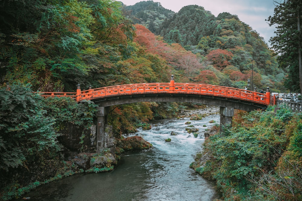 a red bridge over a river surrounded by trees