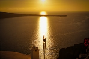 A sleek sailboat gliding past the sunlit cliffs of a Greek island at golden hour