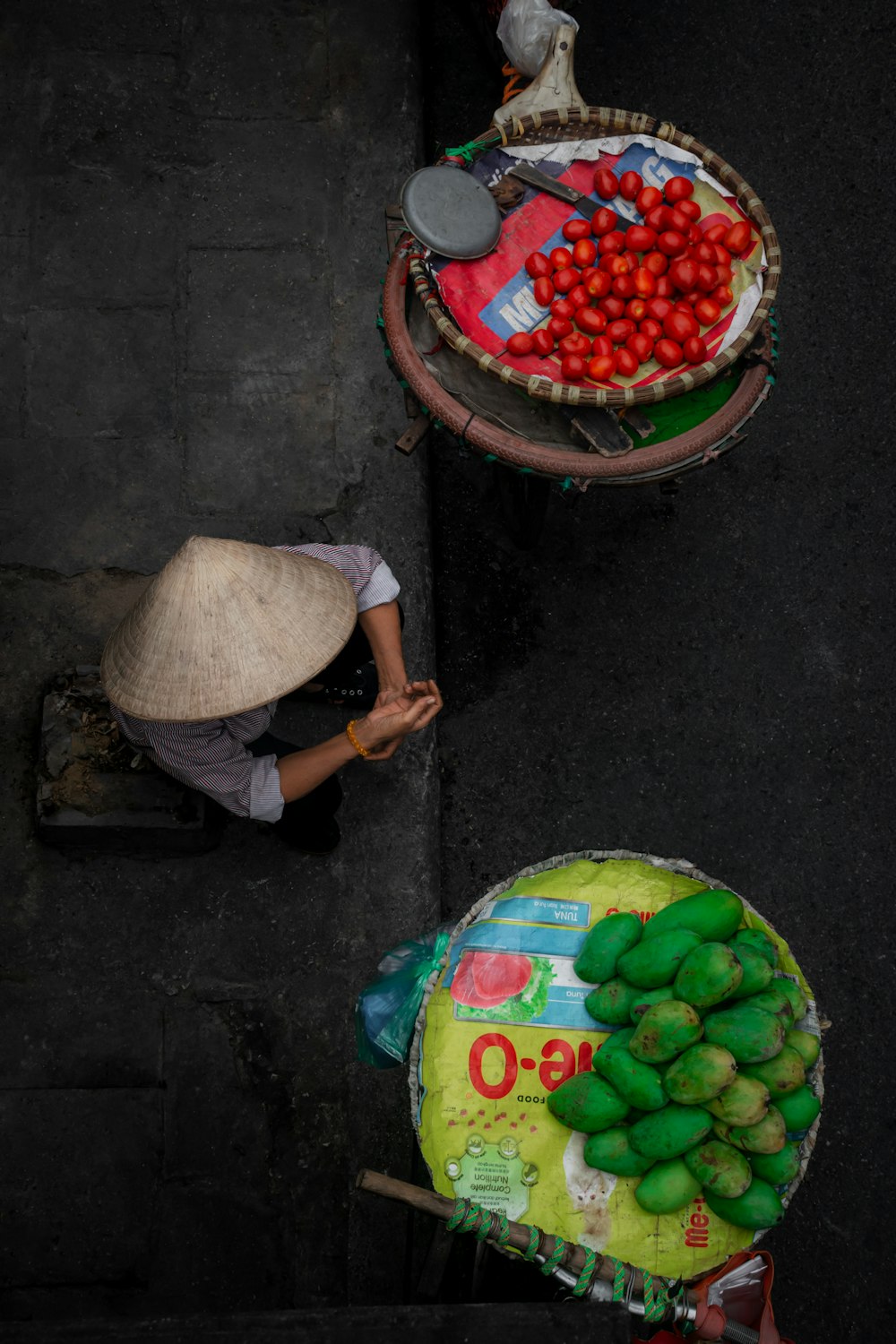 a person with a hat standing next to two baskets of fruit