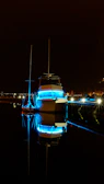 Nighttime shot of an aqua current boat softly illuminated by turquoise LED lights reflecting on calm canal water.