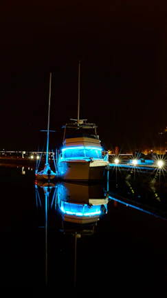 Nighttime shot of an aqua current boat softly illuminated by turquoise LED lights reflecting on calm canal water.